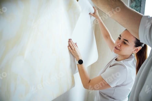 Preview: A middle-aged woman and man paste wallpaper on wall in bright room of house