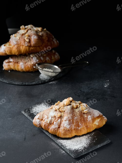 Preview: Baked croissant on a board and sprinkled with powdered sugar, black table.