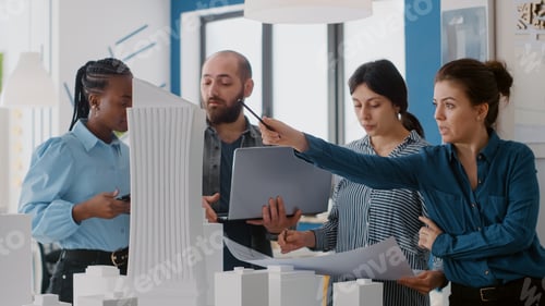 Preview: Close up of colleagues using blueprints, laptop and tablet to design building model for project