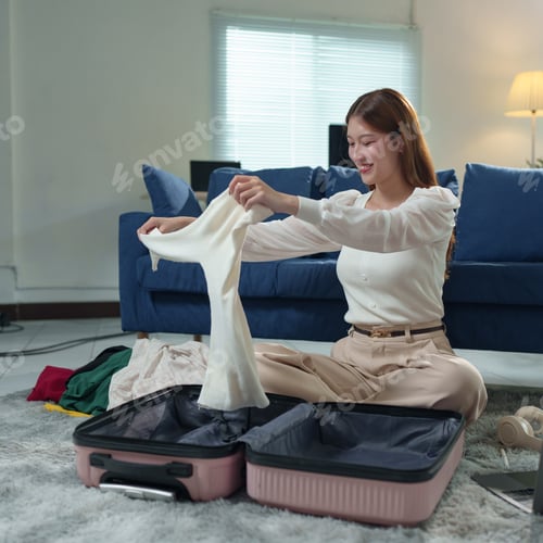 Preview: Happy young asian woman folding clothes and packing a suitcase, preparing for an exciting travel vac