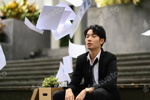 Preview: Shot of depressed businessman sitting on stairs of building and throwing papers in the air