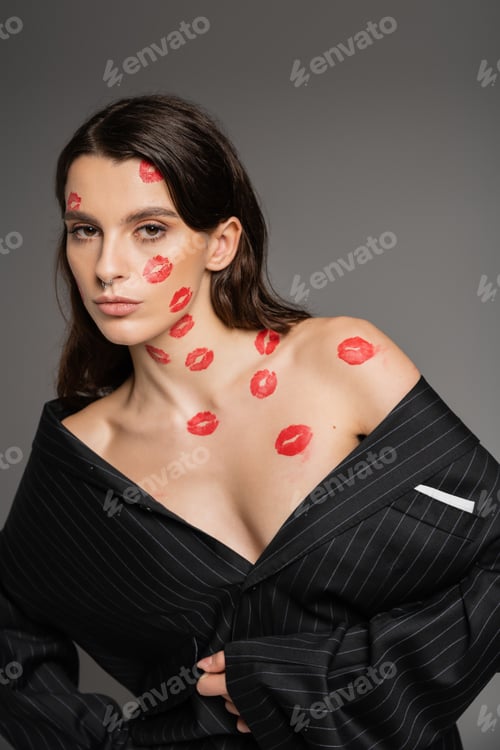 Preview: sensual brunette woman in oversize blazer posing with red kissed on body and face isolated on grey
