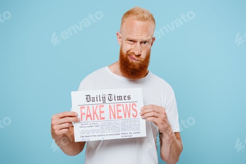 Preview: skeptical bearded man showing newspaper with fake news, isolated on blue