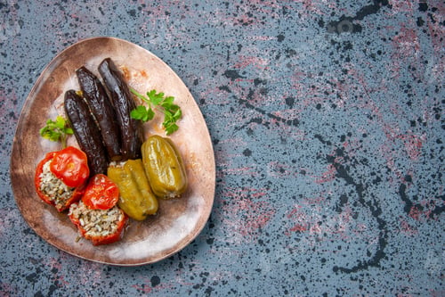 Preview: top view eggplant dolma with cooked tomatoes and bell-peppers filled with ground meat inside plate