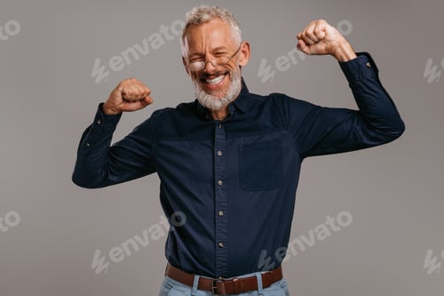 Preview: Happy mature man in smart casual wear celebrating success while gesturing on gray background