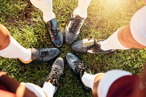 Preview: Shoes, huddle and team on grass field above for sports motivation, coordination or collaboration ou