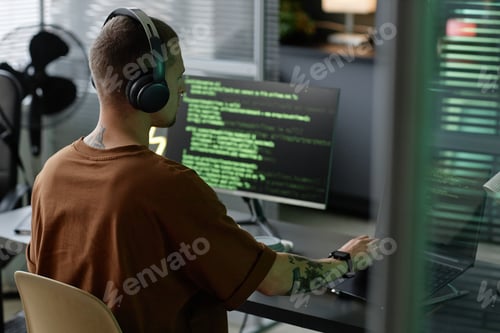 Preview: Male Programmer Wearing Headphones while Using Laptop at Office Workstation