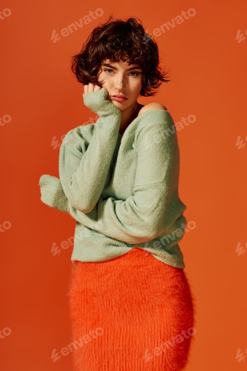 Preview: A young woman expresses deep emotion, standing against a vibrant orange backdrop, in autumn attire