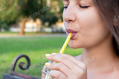 Preview: Young beautiful woman with a bottle of fresh orange juice enjoys a great weather in the park