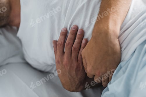 Preview: close-up partial view of man suffering from stomach pain in bed