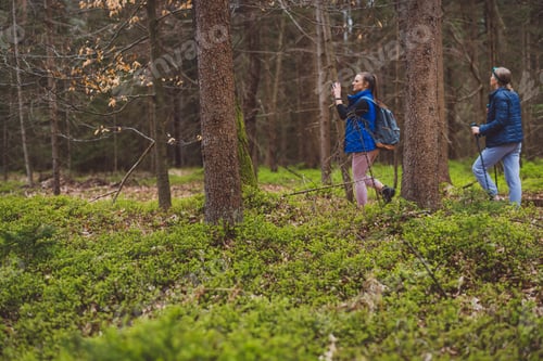 Preview: Two women hiking in a forest, one using trekking poles and wearing a headlamp, the other carrying a