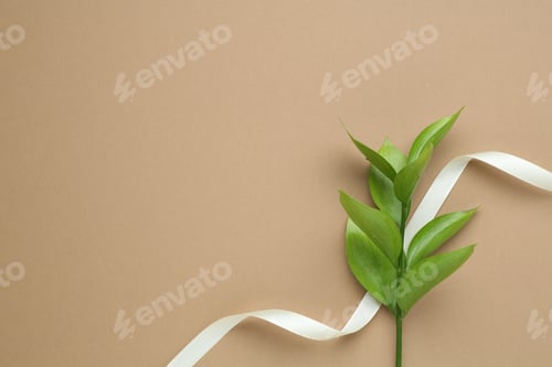 Preview: Beautiful ribbon and green leaves on beige background, flat lay. Space for text