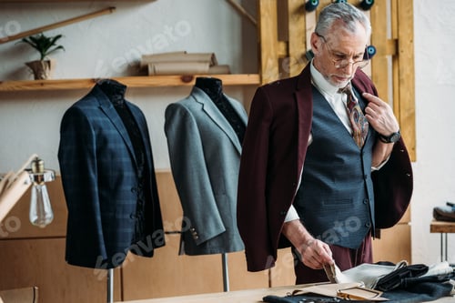 Preview: handsome mature tailor in stylish clothing working at sewing workshop