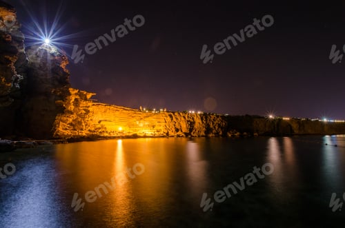 Preview: Nighttime serenity at coastal resort with illuminated rocks