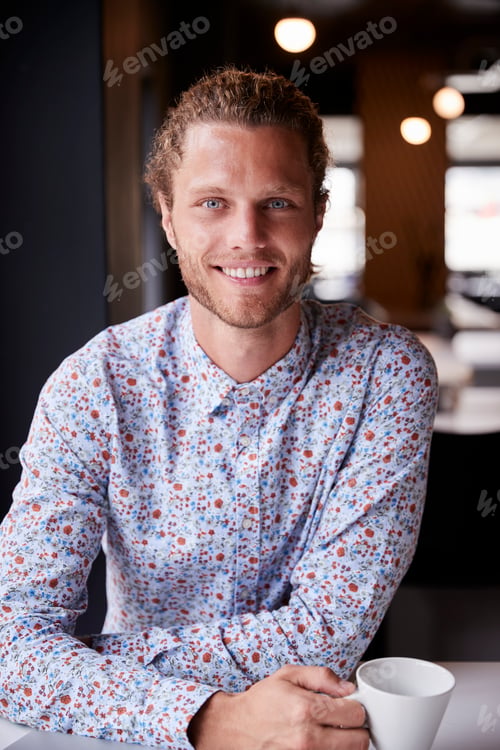 Preview: Millennial white male creative sitting at a desk in an open plan office smiling to camera, vertical