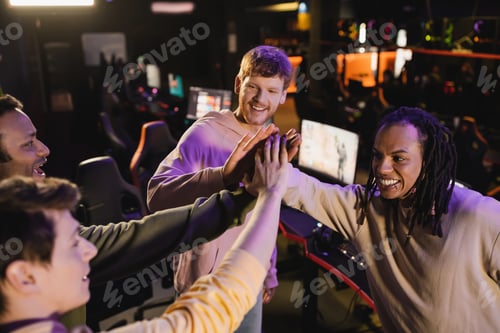 Preview: High angle view of positive multiethnic friends giving high five in gaming club