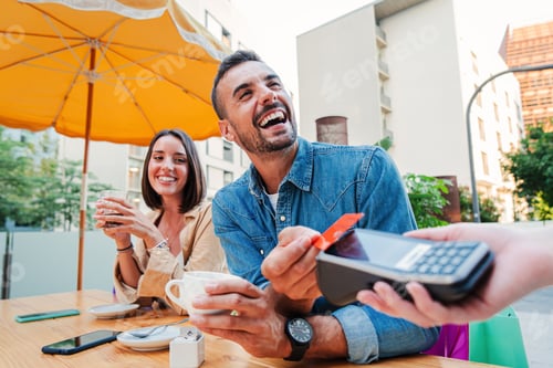 Preview: Happy young adult man paying the bill with a contactless credit card on a restaurant, bar or coffee