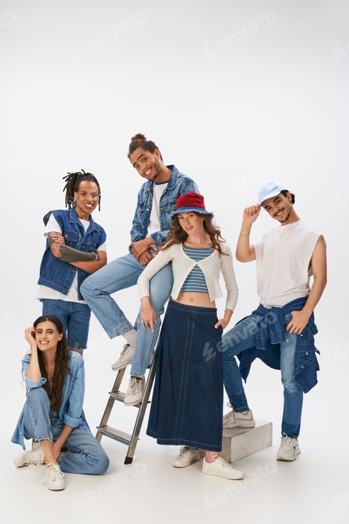 Preview: smiling multiethnic friends in stylish street wear posing with ladder and looking at camera on grey