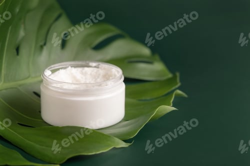 Preview: White jar on monstera leaf on green table close up. Brand packaging mockup