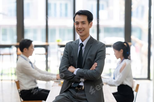 Preview: Confident handsome Asian businessman standing at corporate office and looking at camera.