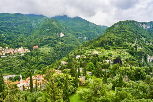 Preview: a lush green hillside with several buildings on it and the mountains in the distance