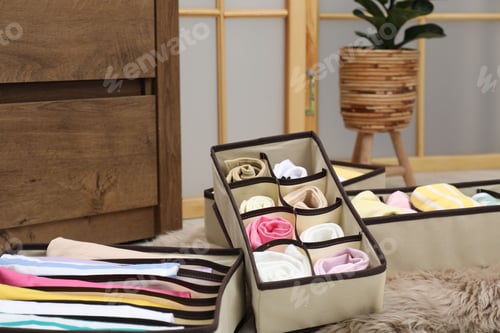 Preview: Organizers with folded clothes on floor indoors, closeup