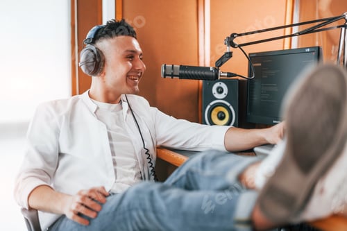 Preview: Talks and uses mic. Young man is indoors in the radio studio is busy by broadcast