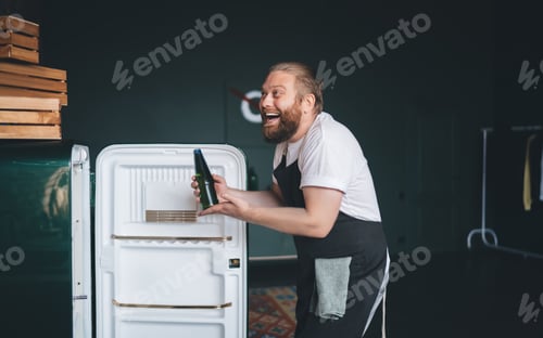 Preview: Man with glass bottle standing at fridge and laughing