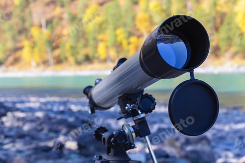 Preview: Gray with black telescope stands on bank of mountain river in autumn, copy space, selective focus