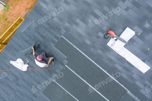 Preview: Professional roofing contractor uses an air nail gun to install new asphalt bitumen shingles on a