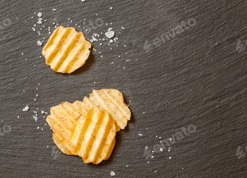Preview: Corrugated potato chips with sea salt on black stone background, top view