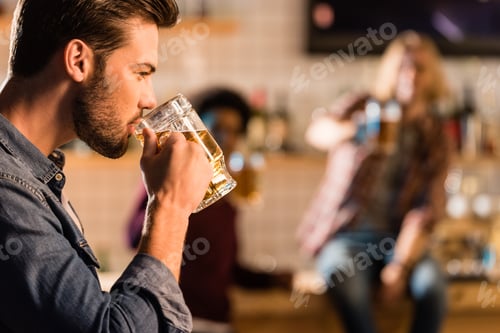 Preview: side view of handsome young man drinking beer in bar
