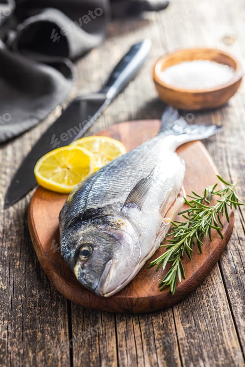 Preview: Fresh sea bream fish on cutting board on wooden table.