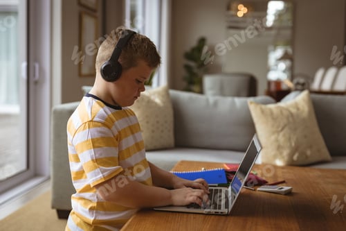 Preview: child typing on laptop in living room near dining area, with headphones and notebooks, copy space