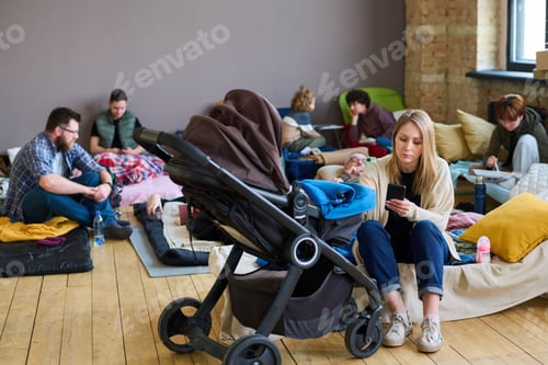 Preview: Young female sitting on couchette by stroller with her baby against refugees