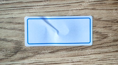 Preview: Blank White Label with Blue Border on a Wooden Background