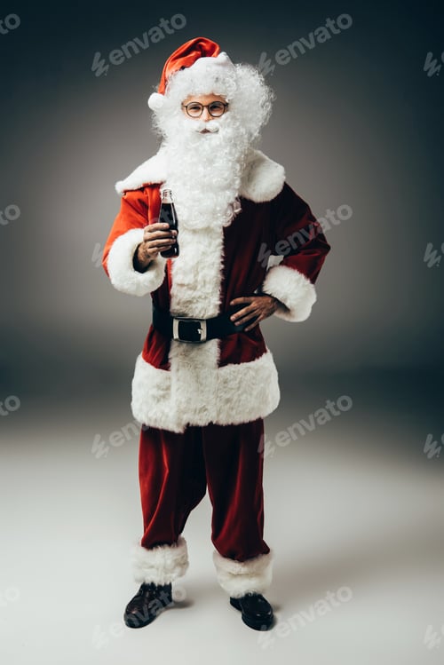 Preview: happy santa claus in costume standing with cream soda bottle on grey background