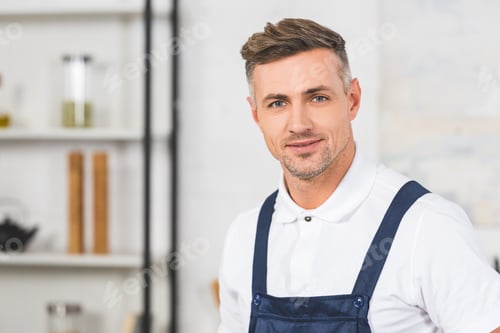 Preview: portrait of adult repairman in overall standing at kitchen and looking at camera