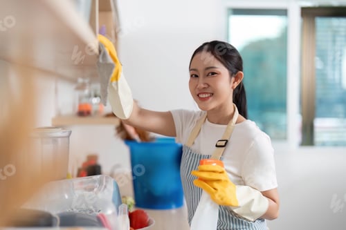 Preview: Home Cleaning. Young woman smiling while organizing kitchen shelves with cleaning supplies.