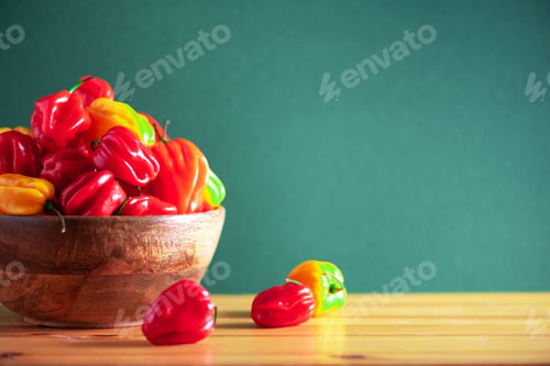 Preview: Colorful scotch bonnet chili peppers in wooden bowl over green background. Copy space