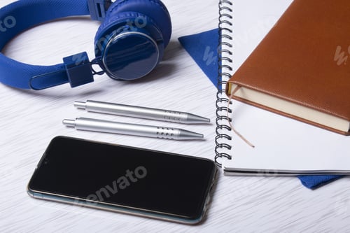 Preview: Top view of a cell phone with headphones, notebooks, and pens on a surface