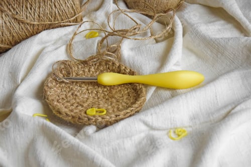 Preview: Handiwork. Natural jute fiber, yellow knitting hook and pins on light fabric.