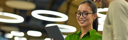 Preview: Young cheerful asian woman showing something on digital tablet to her male colleague while standing