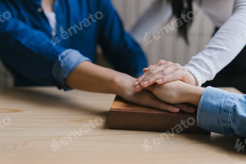 Preview: Friends comforting each other by holding hands on a book on a wooden table