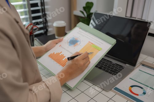 Preview: a businesswoman is sitting in her private office working on her desk with many documents to check