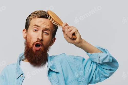 Preview: Portrait of a man with a massage comb in his hands, combing his hair and beard, hair loss problem
