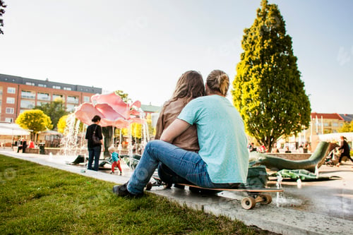Preview: Rear view of couple sitting on skateboard in city park