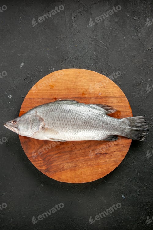 Preview: top view fresh raw fish on round wood board on black table with copy place