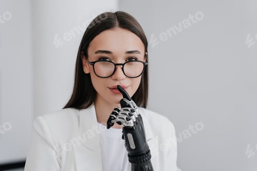 Preview: Keep calm! Handicapped young woman in glasses touches lips by index finger of bionic artificial hand