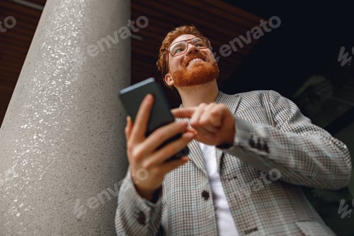 Preview: Bottom view of smiling businessman holding phone while standing near office during break time